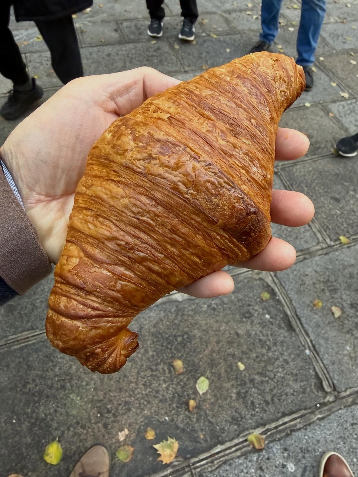 Croissant pur beurre de Tout Autour du Pain tenu en main devant la boutique